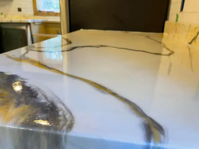 Glossy white epoxy countertop with gold and black veining, close-up