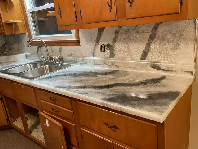 Kitchen countertop and full backsplash finished in white and gray marble-look epoxy under wood cabinets